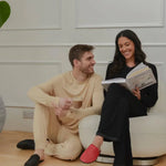 Couple relaxing indoors, man with coffee and woman reading, both in cozy loungewear and slippers