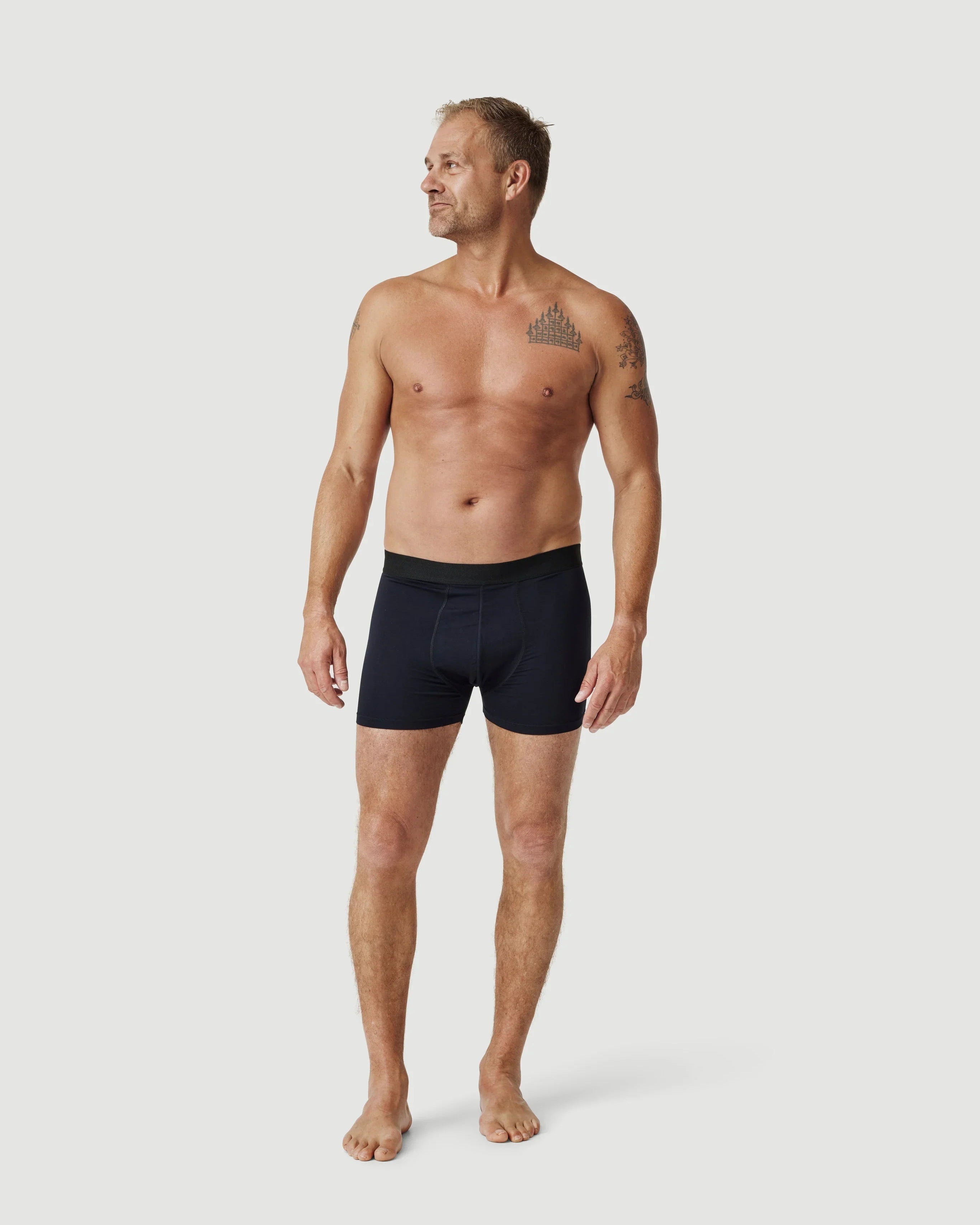 Tattooed man modeling black boxer briefs on plain white background